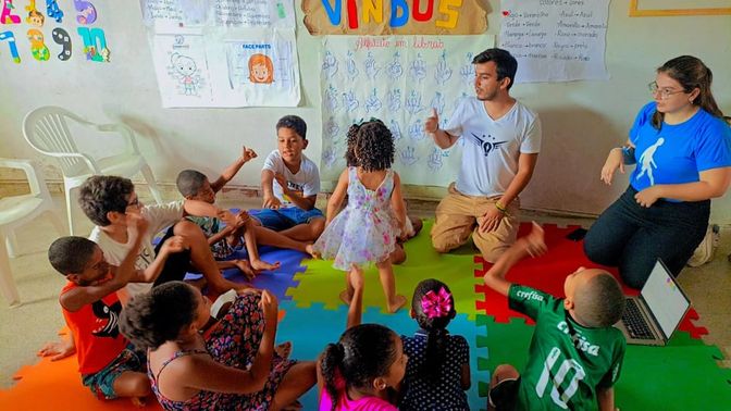 Crianças e voluntários sentados no chão em atividade de educação